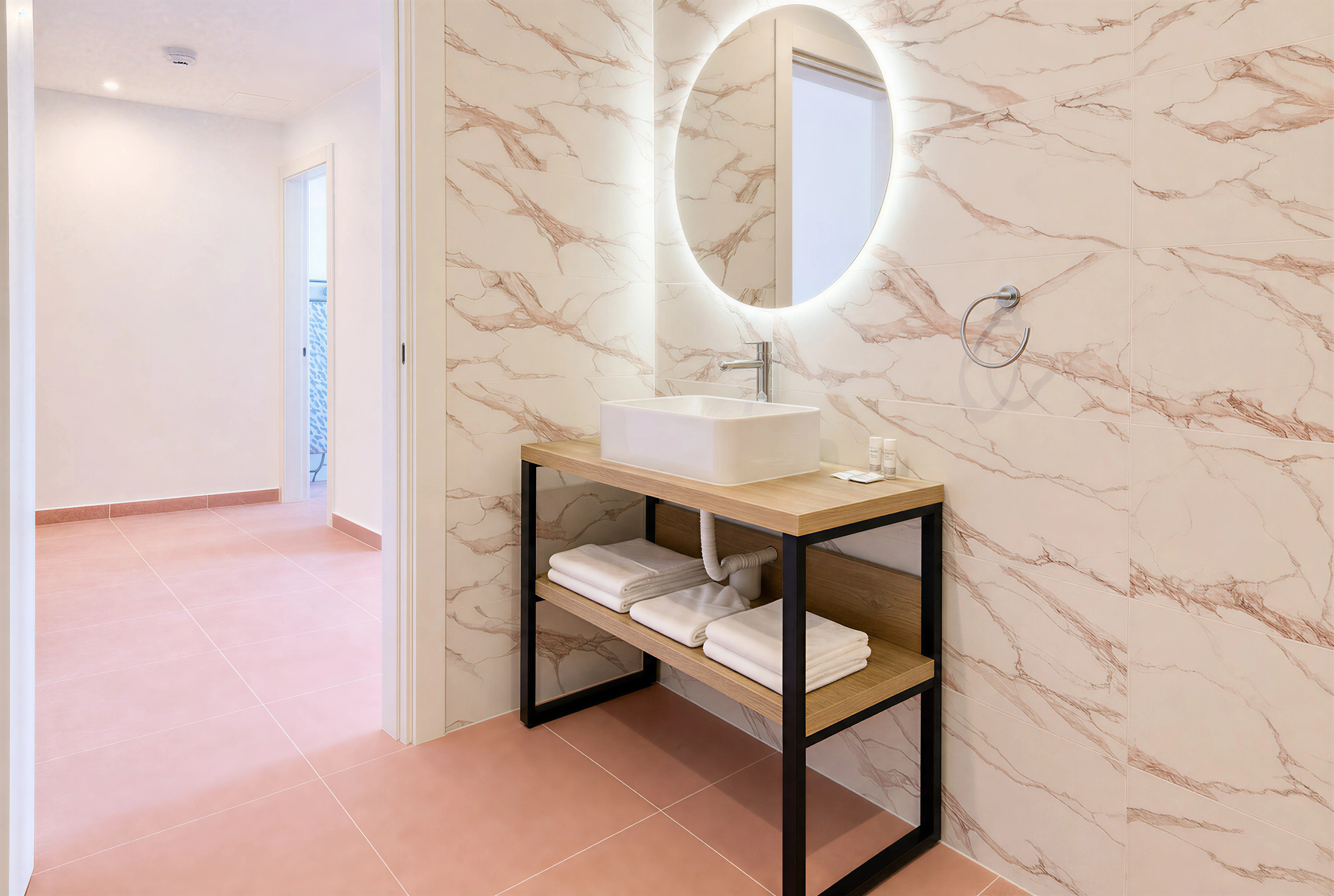 Bathroom with round backlit mirror, vessel sink and pink-veined marble walls at The Flamingo Apartments