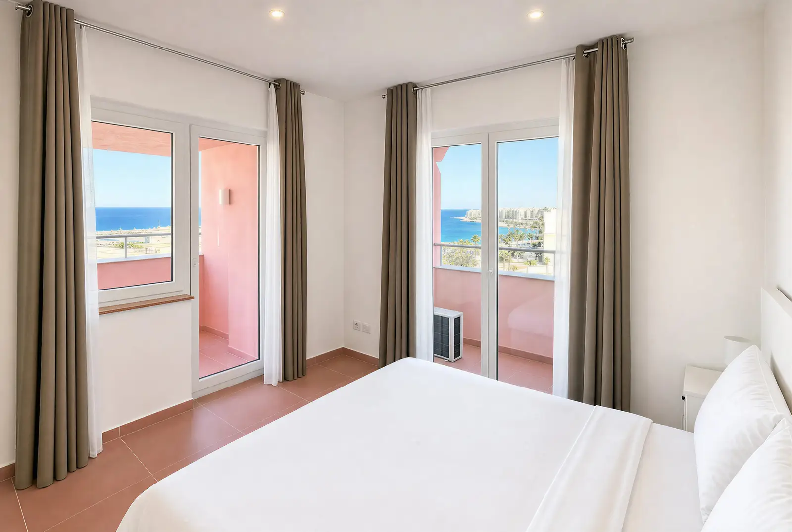 Double bedroom with glass doors to a pink balcony and the sea beyond