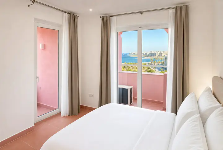 Bedroom with a double bed and two glass doors to a pink balcony