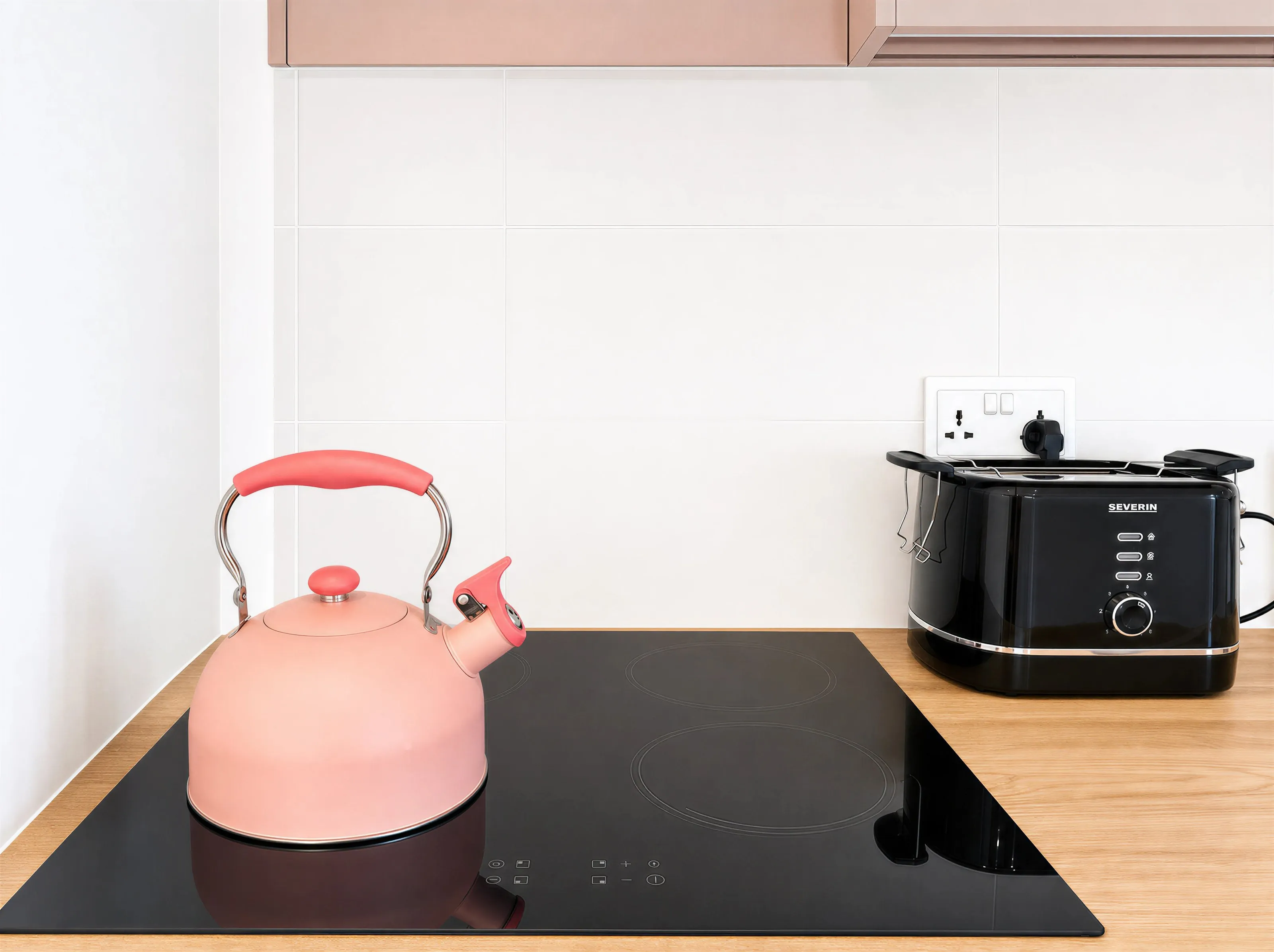 Pink kettle on a black ceramic hob beside a black toaster