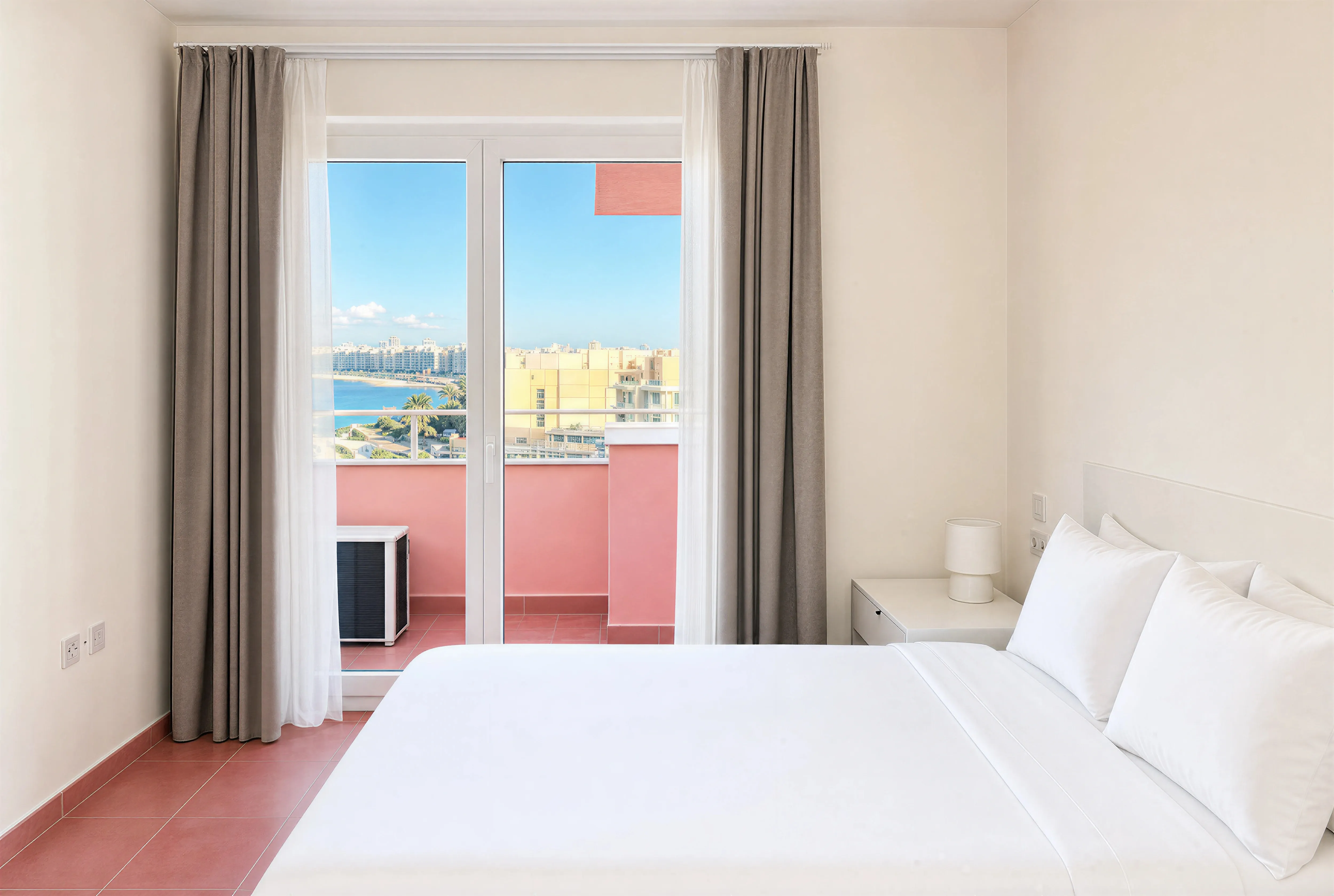 Bedroom with a double bed and glass doors to a pink balcony with sea view