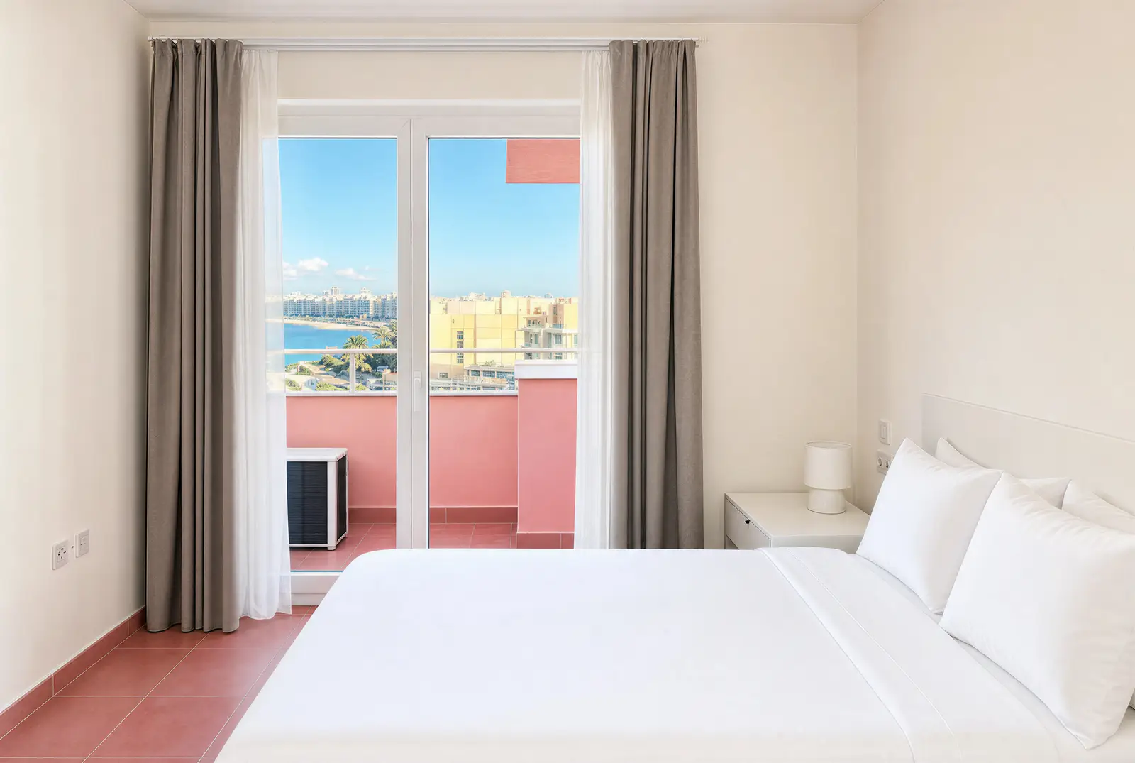 Bedroom with a double bed and glass doors to a pink balcony with sea view