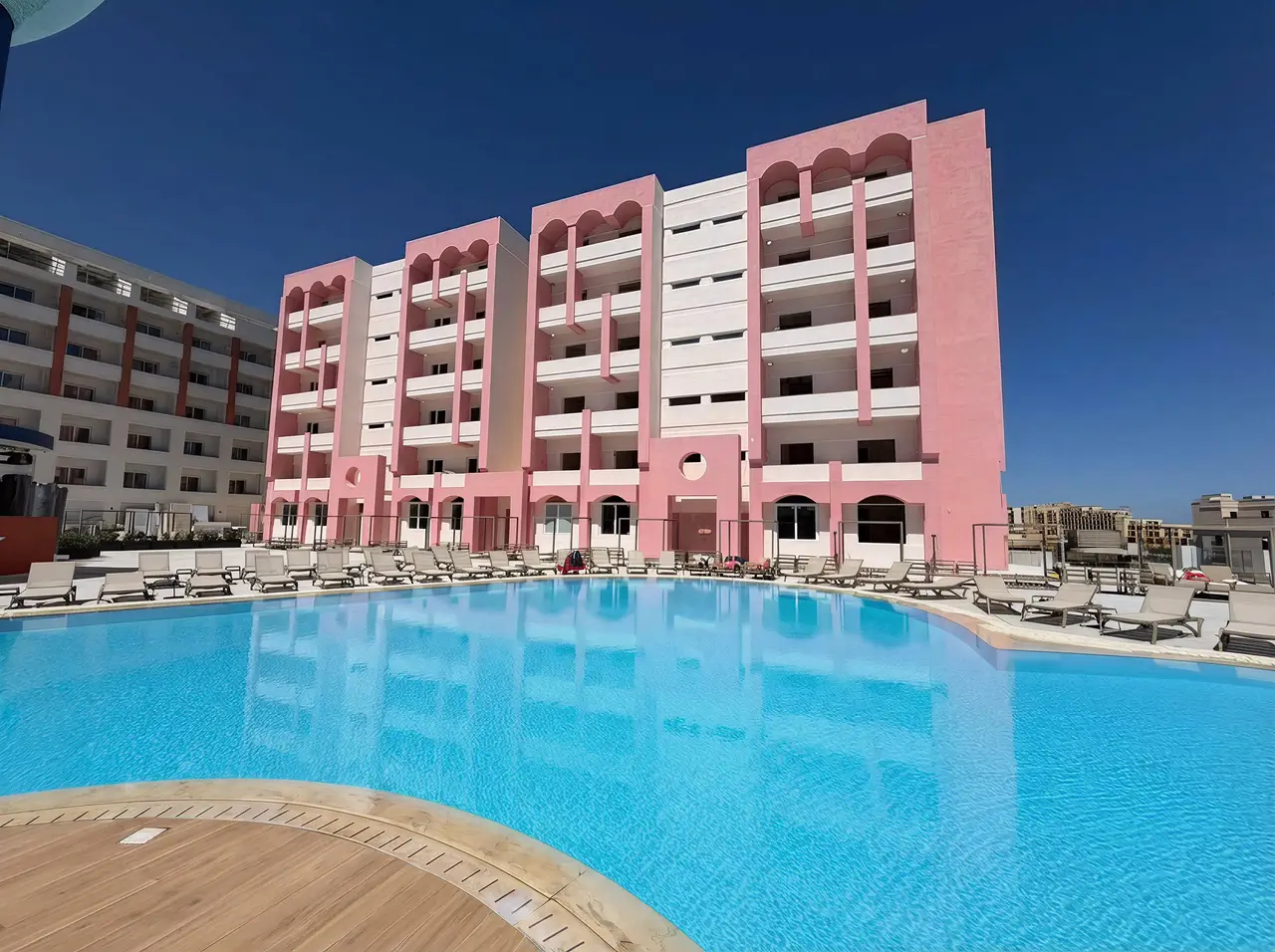 Resort pool lined with sunbeds, the pink-and-white Flamingo Apartments building behind