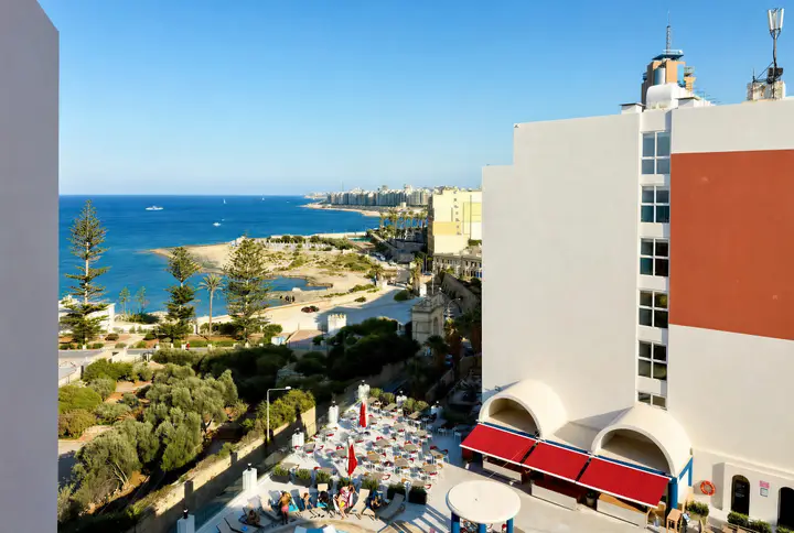 Resort pool deck with sunbeds and red parasols, the sea beyond