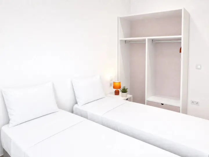 Two single beds with white linen, a bedside lamp and an open wardrobe
